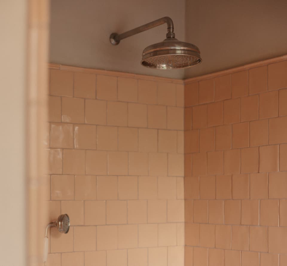 Brass rainfall showerhead in a tiled guesthouse bathroom